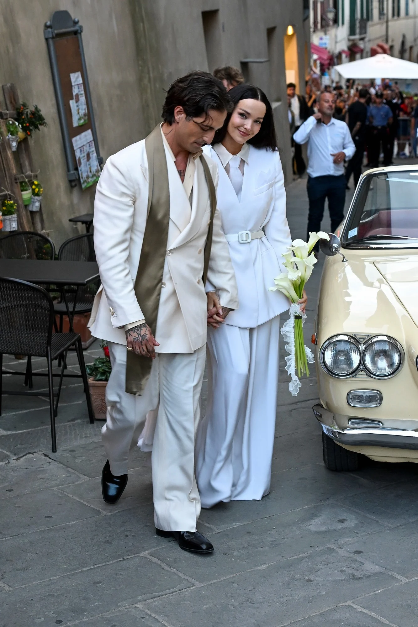 Close-up of Dove Cameron's ivory suit and cape and Damiano David's champagne suit and scarf