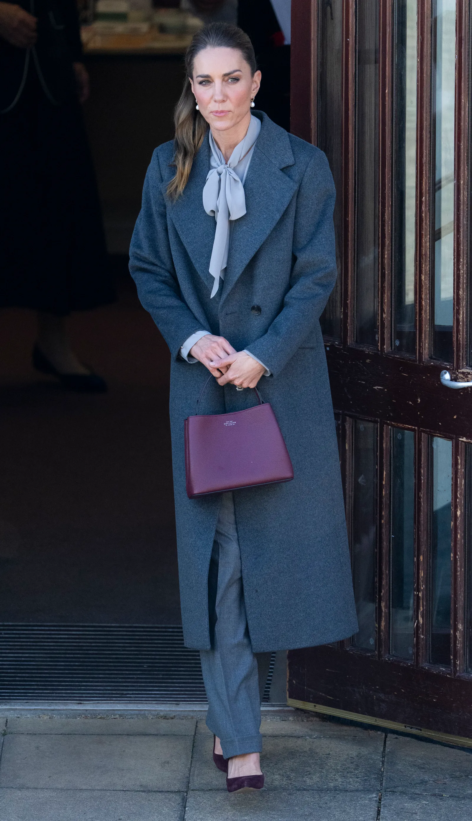 Kate Middleton in a charcoal wool coat, gray blouse and trousers outside West Sussex Minibus